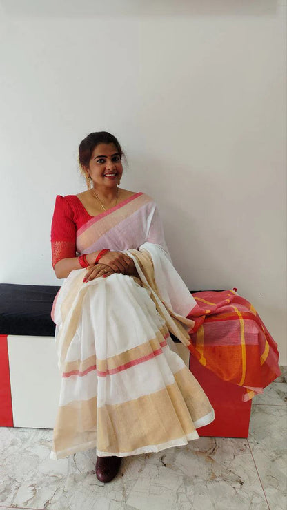 Woman wearing a mul cotton set saree with kasavu border and rich red pallu with tassels sitting on a bench indoors
