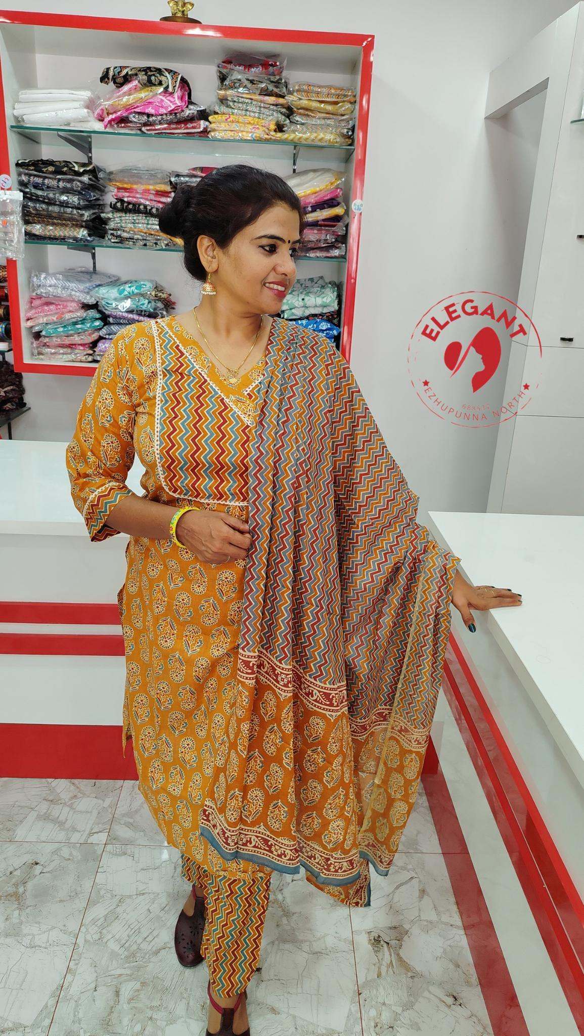 Woman wearing a mustard yellow cotton churidar set with multicolored patterned dupatta in a clothing store.