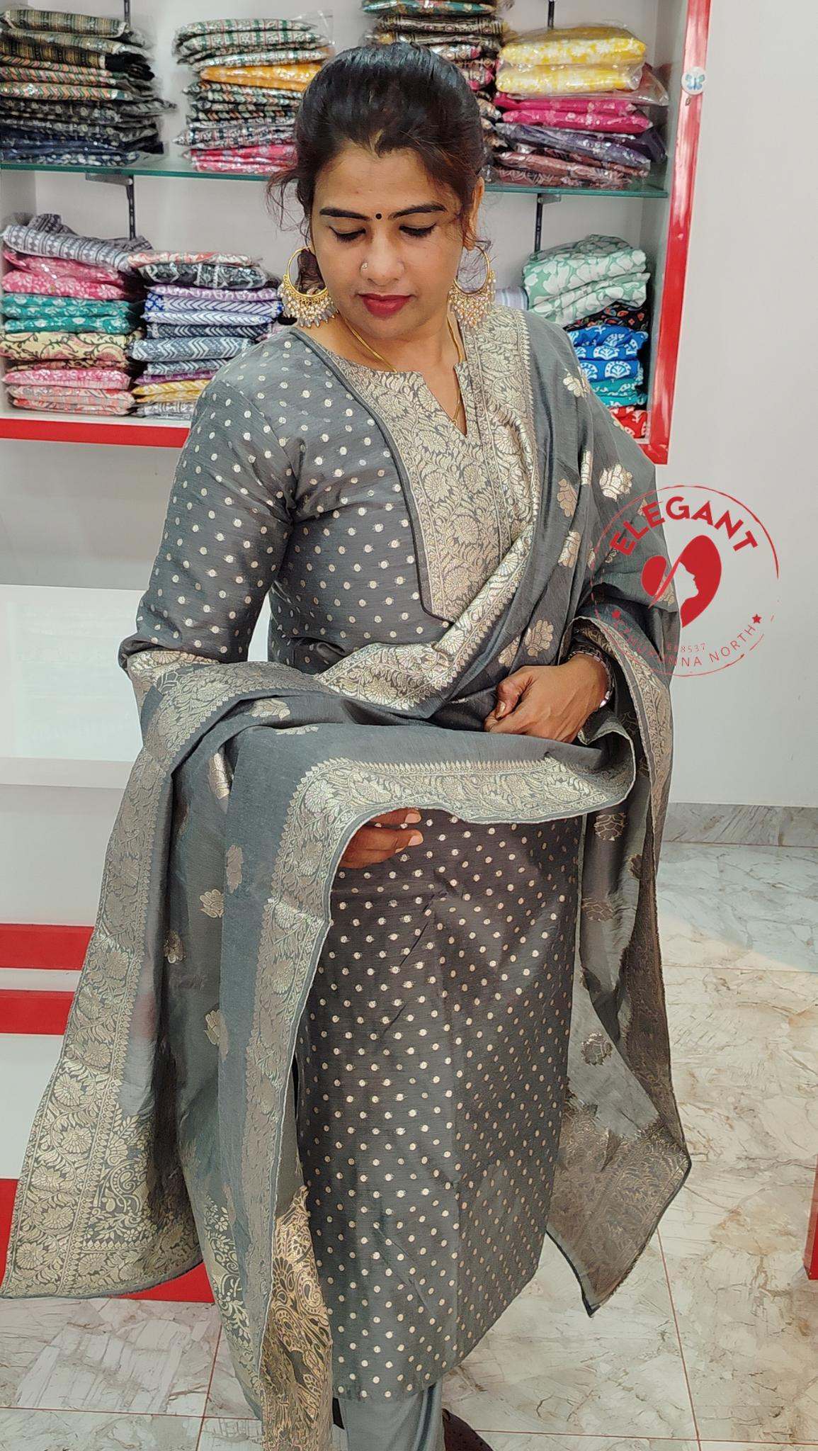 Woman wearing elegant grey silk party wear churidar with intricate gold embroidery in a fabric store setting