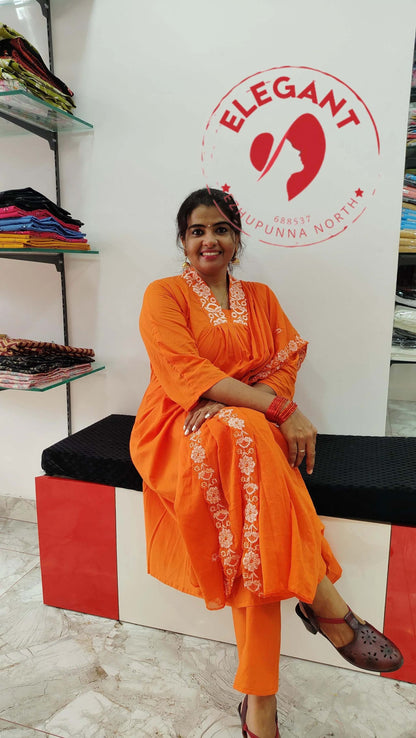 Woman wearing an orange cotton churidar set with white embroidery, sitting on a bench inside a clothing store.