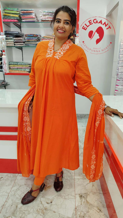 Woman wearing orange cotton churidar set with white embroidery standing in a fabric store with folded textiles in the background