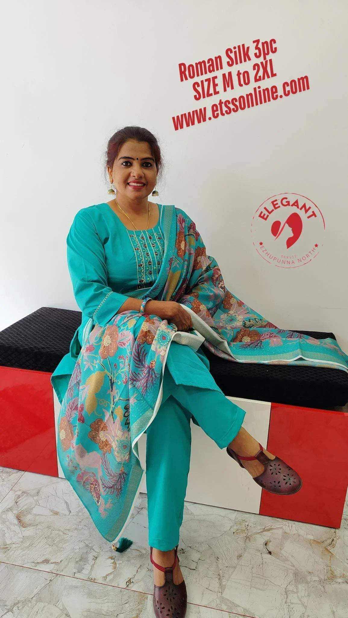 Woman wearing turquoise Roman Silk Churidar with floral patterned dupatta, sitting and smiling indoors
