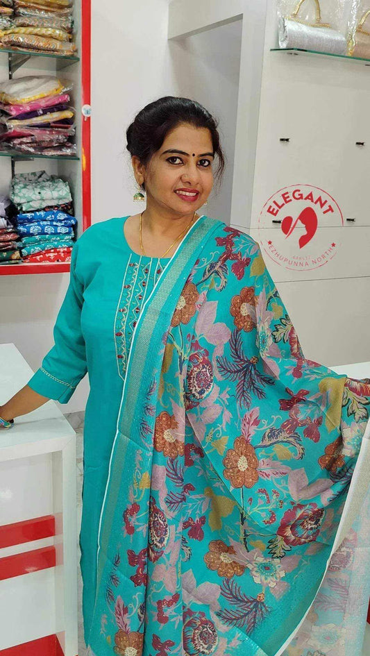 Woman wearing a teal Roman Silk Churidar with floral patterned dupatta in a fabric store interior