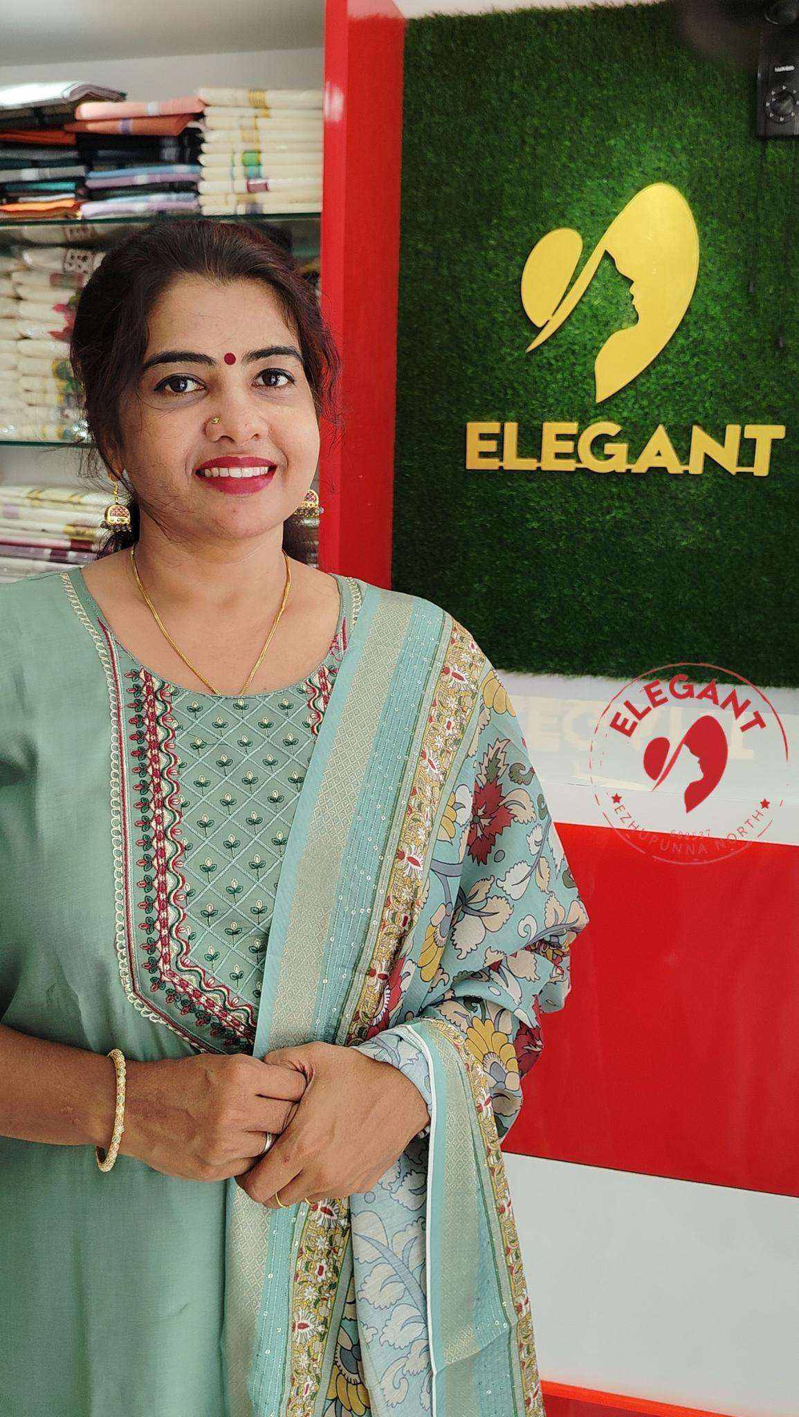 Woman wearing elegant Roman silk churidar in soft green with intricate patterns standing in front of Elegant store sign