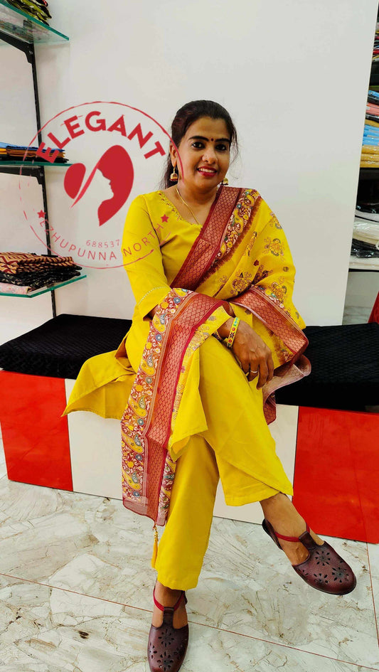 Woman wearing a yellow Roman silk churidar with a patterned red and gold border, sitting indoors on a black and red bench.