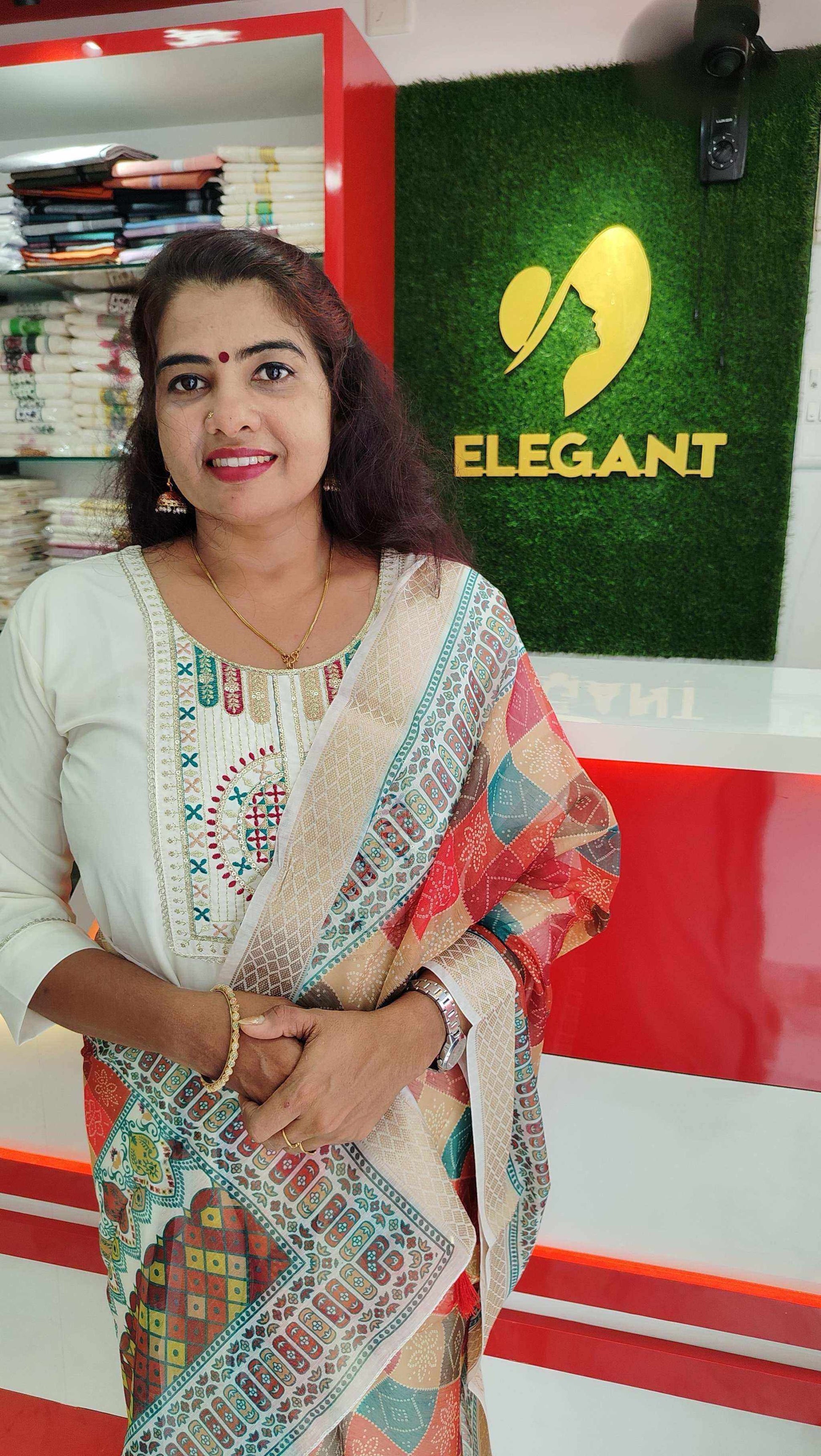 Woman wearing a colorful Roman Silk Churidar standing in front of a store counter with Elegant logo background