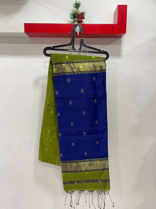 Green and blue saree with gold border on a hanger against a white wall.