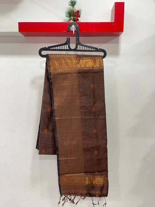 Brown saree with gold patterns on a hanger against a white wall with a red shelf.
