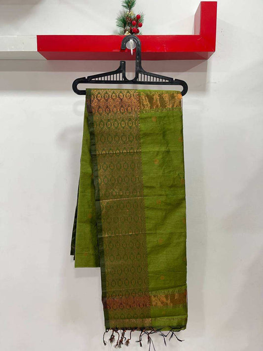 Green saree with brown patterns hanging on a black hanger against a white wall.