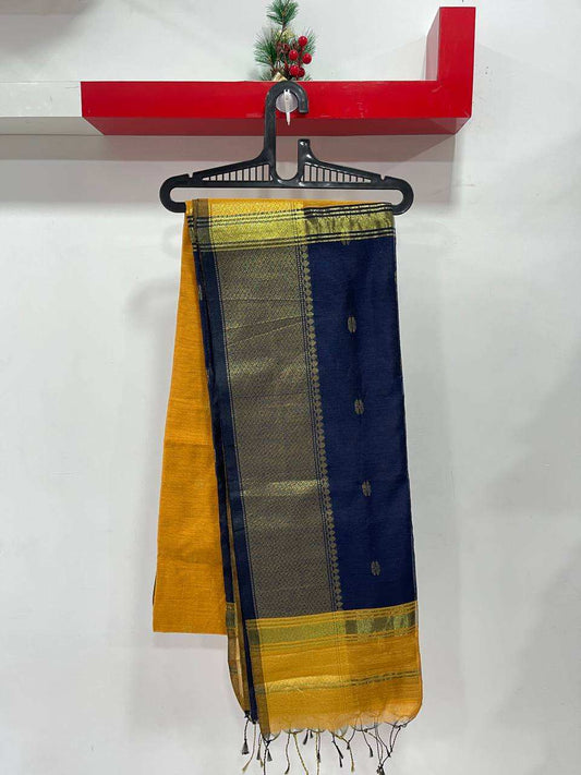 Yellow and blue saree with green border on a hanger against a white wall.