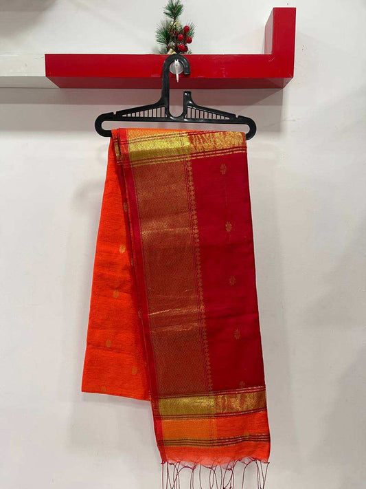 Red and orange saree with gold border on a hanger against a white wall.
