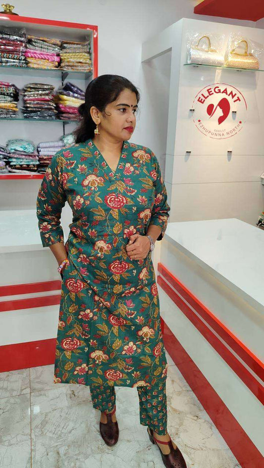 Woman wearing a vibrant green floral kurthi set made of camric cotton, standing in a clothing store.